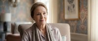 Senior Caucasian businesswoman in elegant beige suit sitting confidently in luxurious office interior, professional executive portrait for corporate communications.