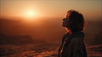 Silhouette of woman with curly hair in profile against golden sunset over mountain landscape, peaceful contemplative moment in nature.