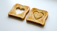 Two golden toasted bread slices with heart-shaped cutouts on white background, perfect for romantic breakfast, Valentine's Day meal or love-themed food concepts.