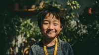 Young Asian boy with cheerful smile wearing gray sweater and yellow lanyard in lush green garden setting for educational and lifestyle content.