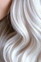 Luxurious platinum blonde wavy hair texture closeup showing smooth, silky strands with gentle curves and natural shine against neutral background.