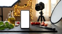 Food photography setup with blank smartphone screen, fresh ingredients and professional camera equipment for culinary content creation and recipe blogging.