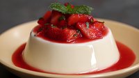 Creamy panna cotta dessert topped with fresh strawberries and mint leaves on elegant plate with berry sauce for gourmet dining and culinary presentations.