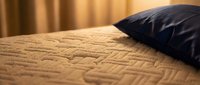 Beige quilted bedding with dark navy pillow on warm-toned bed, suitable for home decor, interior design, and bedroom styling projects.