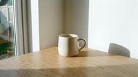 Ceramic mug on wooden table near window with natural light, minimalist interior design setting for home decor and lifestyle content.
