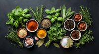 Fresh herbs and colorful spices arranged on dark slate background. Culinary ingredients including basil, rosemary, thyme with various seasonings in bowls.