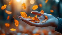 Female hand gently catching falling autumn leaves against blurred forest background with golden bokeh lights, creating magical seasonal atmosphere.