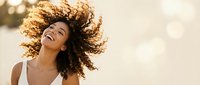 Young African American woman with curly hair dancing joyfully in golden sunlight, expressing freedom and happiness with flowing movement and radiant smile.