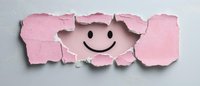 Smiling face revealed through torn pink paper on white background, creating positive emotional breakthrough concept for mental health and happiness themes.