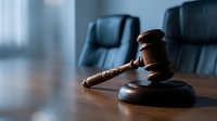 Wooden gavel on polished table in modern courtroom with leather chairs, symbolizing justice, law, legal proceedings, and judicial authority.
