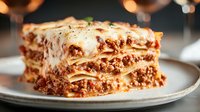 Homemade lasagna slice with melted cheese, meat sauce and pasta layers on white plate. Traditional Italian comfort food for restaurant menus and cooking blogs.
