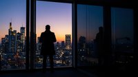 Silhouettes of two businesspeople standing at floor-to-ceiling windows overlooking illuminated city skyline at dusk, suitable for corporate and business concepts.