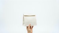 Hand holding blank white paper bag against light background for shopping, packaging, branding and retail mockup designs.