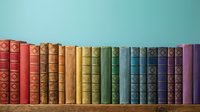 Row of colorful vintage books arranged by color spectrum from red to purple on wooden shelf against turquoise wall for library and education concepts.