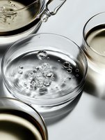 Bubbles and droplets floating in clear liquid inside laboratory petri dish on white background, macro photography with selective focus and reflections.