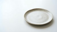 Empty ceramic plate with speckled glaze on white background, minimalist tableware for food presentation and kitchen styling projects.