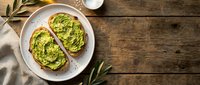 Avocado toast on sourdough bread with herbs and olive oil served on white plate, healthy breakfast meal on rustic wooden table background with copy space.