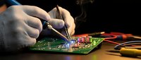 Technician repairing electronic circuit board with soldering iron in workshop. Professional electronics repair and maintenance service for computer hardware components.
