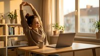 Young woman stretching arms above head while working at laptop in bright home office with plants and warm sunlight streaming through window.