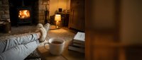 Cozy winter evening at home with feet in warm slippers resting near a fireplace, a hot tea cup on the floor, soft lighting.
