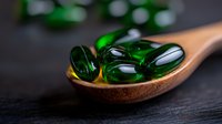 Green translucent soft gel capsules on wooden spoon against dark background, macro photography highlighting pharmaceutical supplements with selective focus.