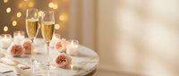 Two champagne flutes filled with sparkling wine on elegant table with pink roses and warm bokeh lights creating romantic celebration atmosphere.