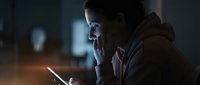 Man wearing glasses using smartphone at night in dark office environment with blurred city lights in background, suitable for technology, business, and communication concepts.