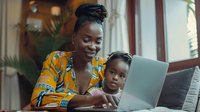 African American mother and child looking at laptop screen together, sharing positive moment while working from home in casual setting with natural lighting.