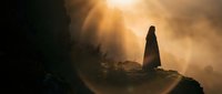 Silhouette of woman standing on mountain cliff edge during golden sunset with dramatic light rays breaking through clouds creating spiritual atmosphere.