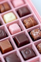 Assorted luxury chocolate pralines and truffles in pink box with dark, milk, and white chocolate varieties decorated with sea salt and cocoa powder.
