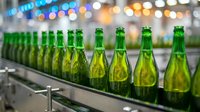 Row of green glass bottles filled with golden champagne or sparkling wine on production line with blurred bokeh lights in background, suitable for beverage industry, winery marketing, and alcohol packaging.