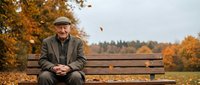 Elderly Caucasian man in vintage suit and cap sitting on park bench during autumn season with golden foliage and falling leaves creating peaceful retirement moment.