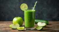 Fresh green smoothie with apple slices and lime garnish on rustic wooden table. Healthy detox drink with striped straw for wellness and nutrition lifestyle.