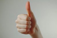 Close-up view of pale caucasian hand showing thumbs up gesture against light gray background, expressing positivity, agreement and approval.