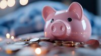 Pink ceramic piggy bank on scattered coins with soft bokeh lights in background, representing savings and financial planning concept.