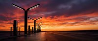 Street lamps illuminate an empty road at sunset with dramatic orange and purple clouds reflecting on wet pavement, suitable for backgrounds and atmospheric scenes.
