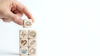 Hand placing wooden cube with lotus symbol on stack of healthcare icons representing wellness and mindfulness practices for holistic health.