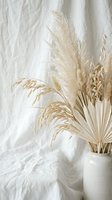 Dried pampas grass and palm leaves in ceramic vase against white linen backdrop creating minimalist boho home decor arrangement for interior design projects.