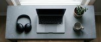 Minimalist home office desk setup with laptop, wireless headphones, coffee mug, and small plant on marble surface, top view.