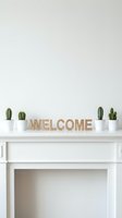 Minimalist white fireplace mantel with wooden welcome sign and small potted cacti, clean Scandinavian home decor interior styling.