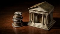 Classical bank building model with stacked coins on wooden surface representing financial institution, savings, investment and monetary system concepts.