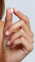 Female hand holding transparent hydrogel skincare capsule between fingers against neutral background, showcasing beauty product for cosmetic advertising.