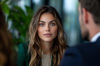 Young businesswoman with highlighted brown hair and natural makeup wearing emerald green blazer during office meeting, professional corporate portrait.
