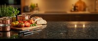 Fresh ingredients and copper cookware arranged on granite countertop in modern kitchen interior with warm lighting and herbs for culinary preparation.