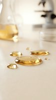 Golden liquid droplets and capsules arranged on white surface with laboratory equipment blurred in background, representing vitamins, supplements, and wellness products for healthcare and pharmaceutical use.