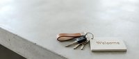 Keys with a leather strap and a wooden welcome tag resting on a concrete surface, symbolizing new home ownership or rental property.