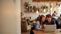 Young couple working together on laptop in cozy modern cafe with warm lighting and industrial decor for remote work and collaboration.