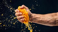 Hand squeezing orange with juice splashing against dark background. Dynamic citrus fruit action shot for beverage, health and food advertising campaigns.
