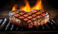 Juicy heart-shaped beef steak grilling on barbecue with flames in background, perfect for restaurant menu or food advertising.