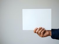 Male hand with medium skin tone holding blank white card or paper against neutral background for messaging or advertising purposes.